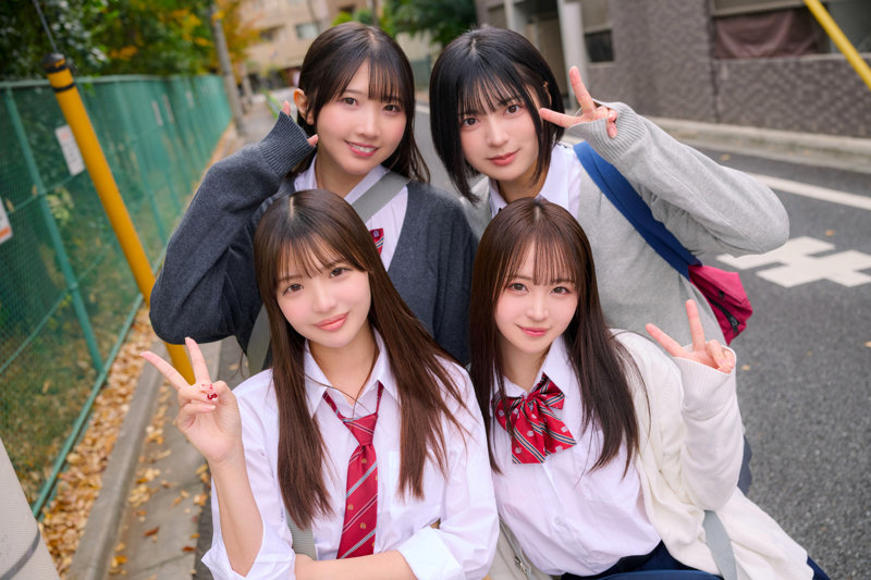 通学路で制服姿の4人組が前列と後列に分かれ、肩を寄せてカメラを見る