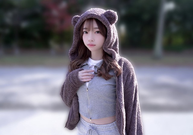 クマ耳フードの女性が公園のような屋外で立ち、カメラを見る