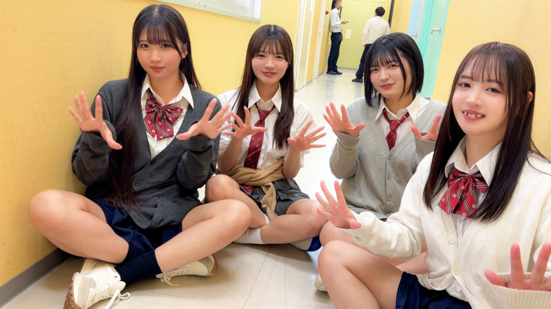 制服姿の4人組が廊下に横並びで座り、両手を前に出して笑顔で並ぶ